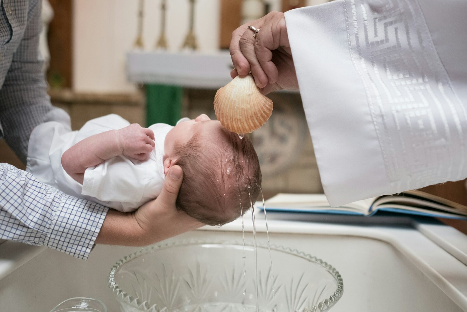 Baby being christened with water poured from a shell over the font